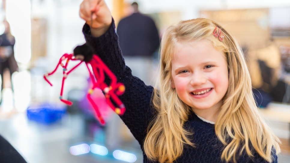 Girl holding a Halloween spider craft made from pipe-cleaners.