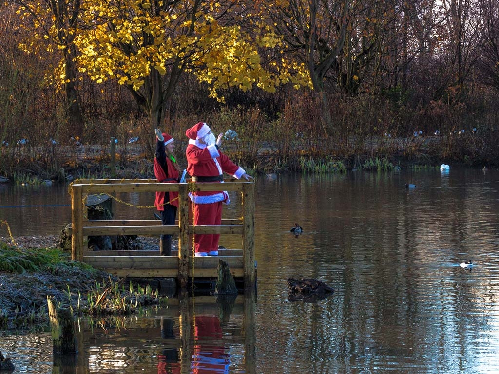 Santa and an elf stand on a boardwalk, waving and welcoming visitors.