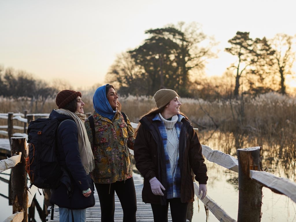 Three friends in winter clothes walking through wetlands.